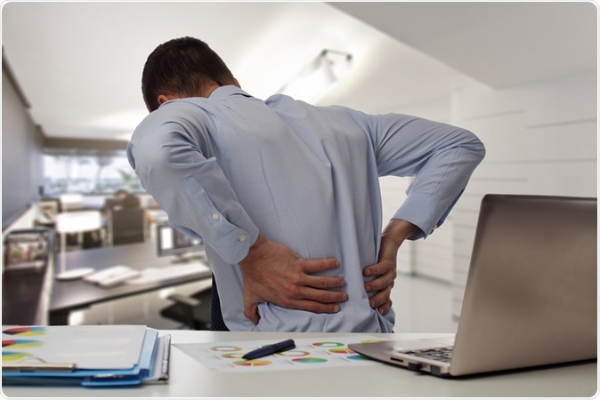 Business man with back pain sin an office . Pain relief concept. Image Credit: Albina Glisic / Shutterstock