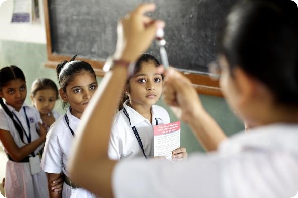 Girls who are waiting to be immunized watch as a vaccinator fills a syringe with measles vaccine, during an immunization session at Deewan Ballubhai school in the Paldi neighbourhood of the city of Ahmedabad in Gujarat State. Children over age 5 are being vaccinated in schools during the SIA campaign against measles. Six vaccination teams from the Paldi health centre – each consisting of a vaccinator, a community volunteer, an anganwadi worker and a schoolteacher or community worker; and overseen by a supervisor – immunized more than 890 children between 5 and 10 years of age at the private school.