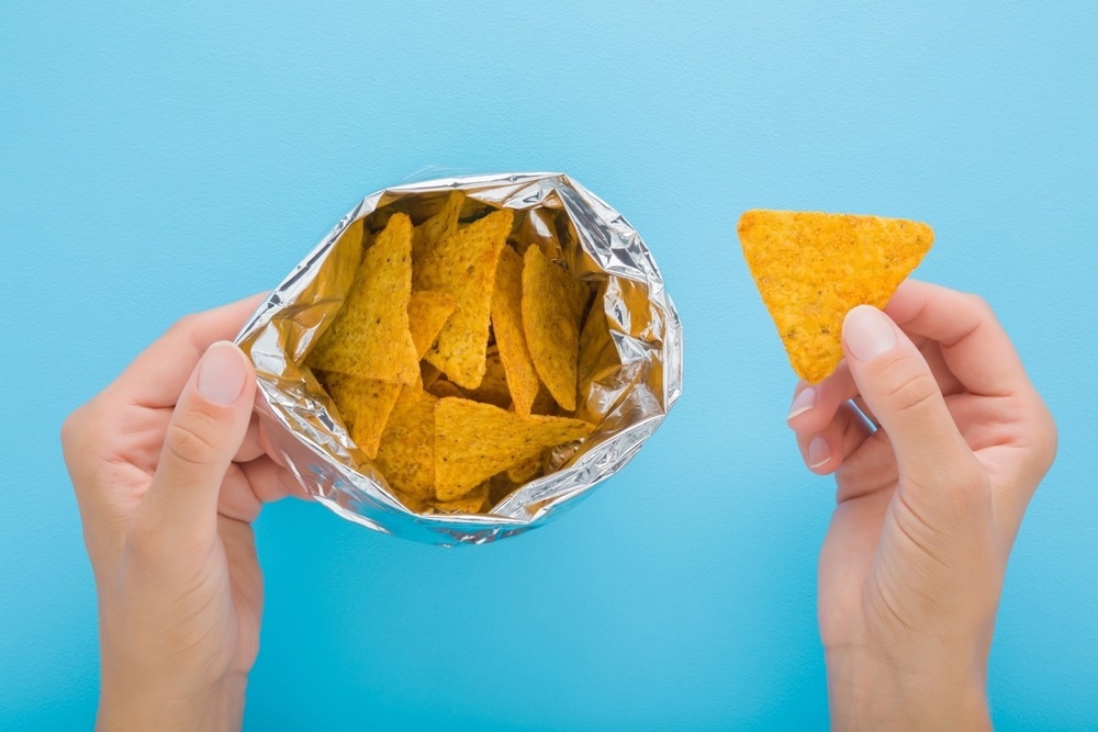 Corn undergoes various stages of processing across the NOVA categories: starting from fresh corn kernels (Category 1), which are unprocessed or minimally processed. It can then be processed into corn oil or cornstarch (Category 2) as culinary ingredients. Further processing turns corn into products like canned corn or corn tortillas (Category 3). Finally, highly processed items like the corn chips in the image, containing additives and industrial modifications, fall into Category 4—ultra-processed foods. Image Credit: FotoDuets/Shutterstock.com