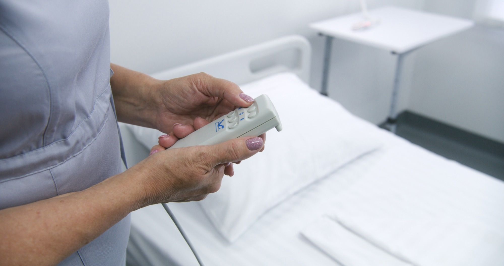 Mature nurse adjusts smart bed in hospital ward using lifting remote control.