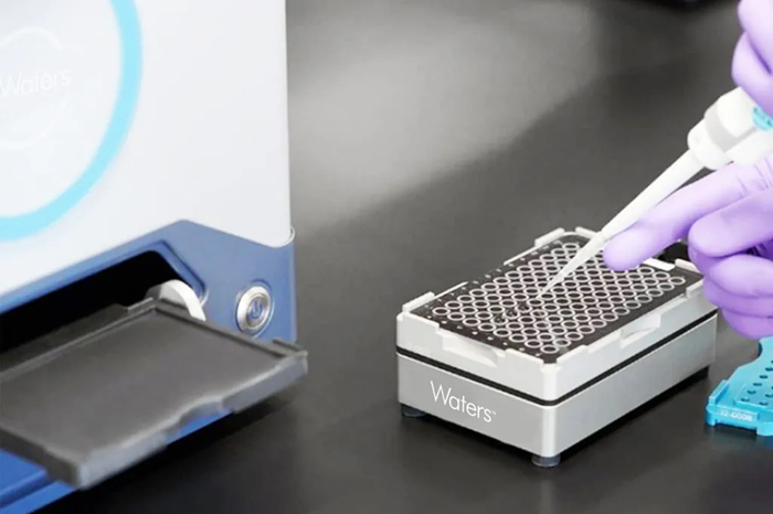 A scientist uses a micropipette with a Waters sample holder.