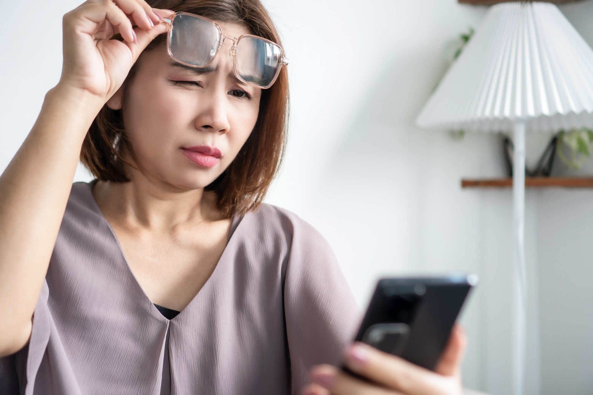Woman trying to read small text on her mobile screen, squinting and holding the phone at a distance