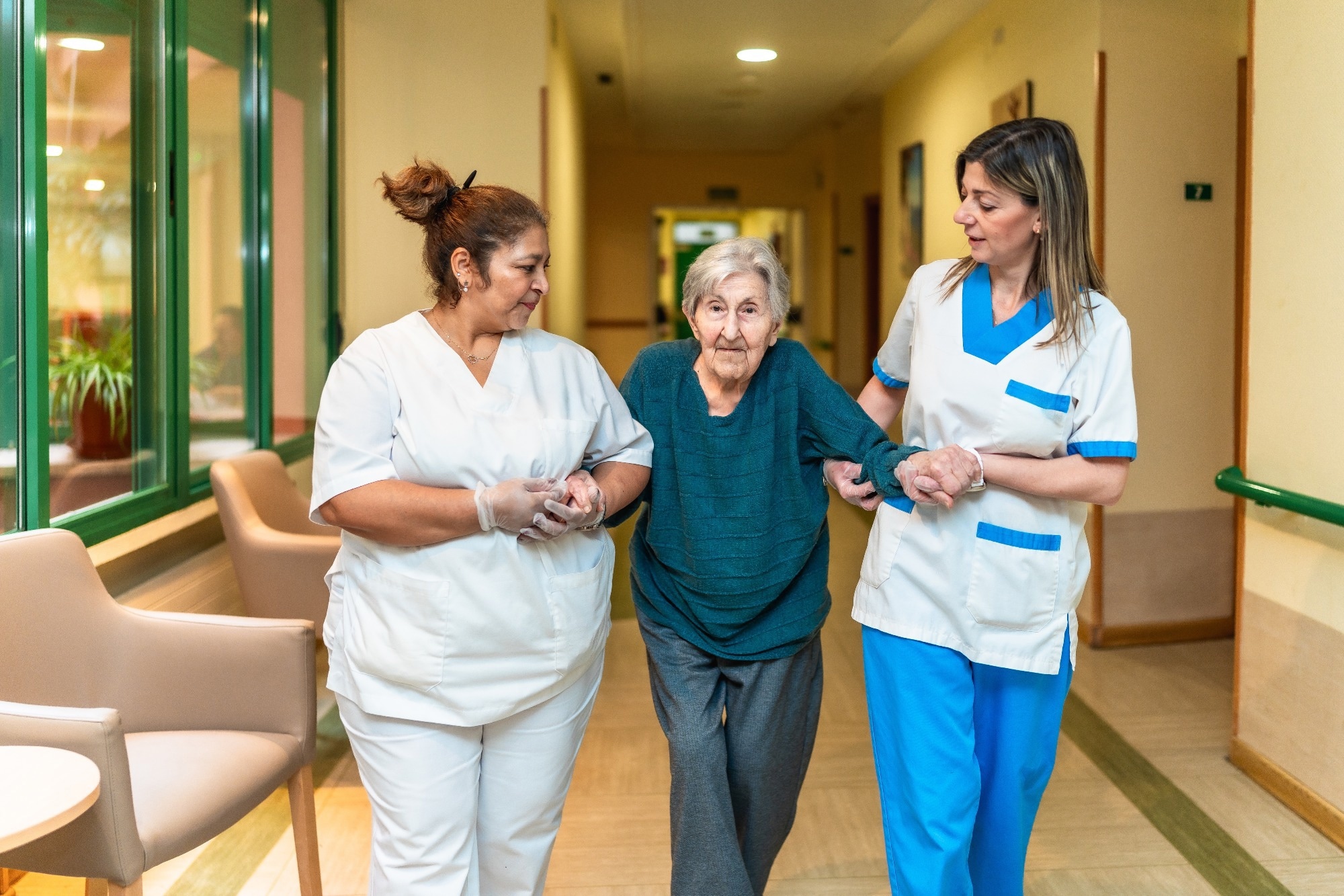 Two nurses assisting an elderly woman walking