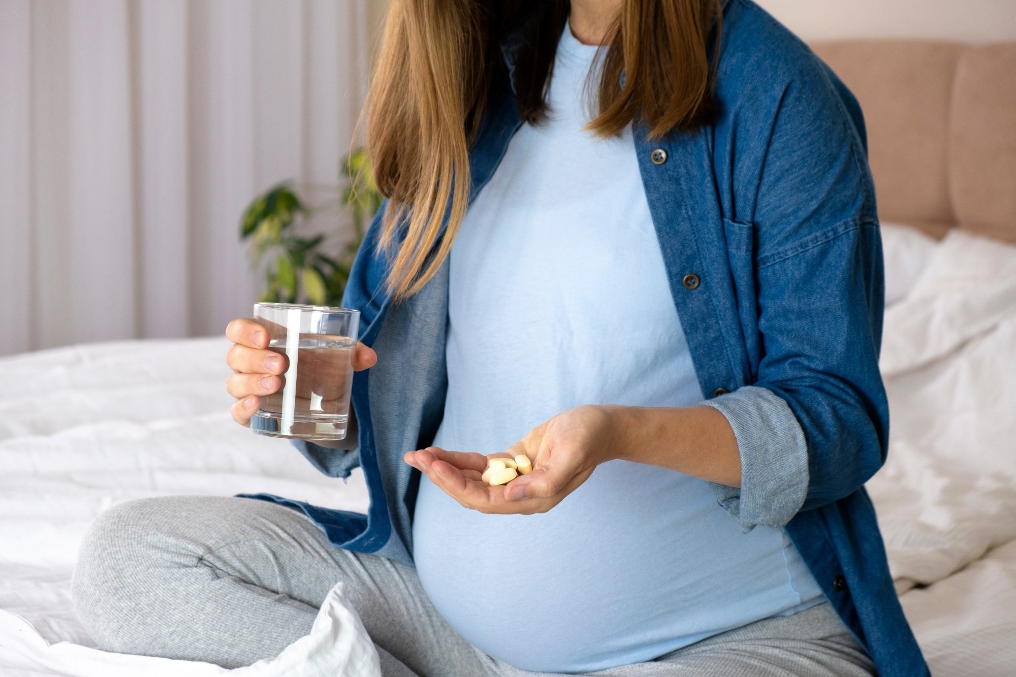Pregnant woman hold pills and glass of water.