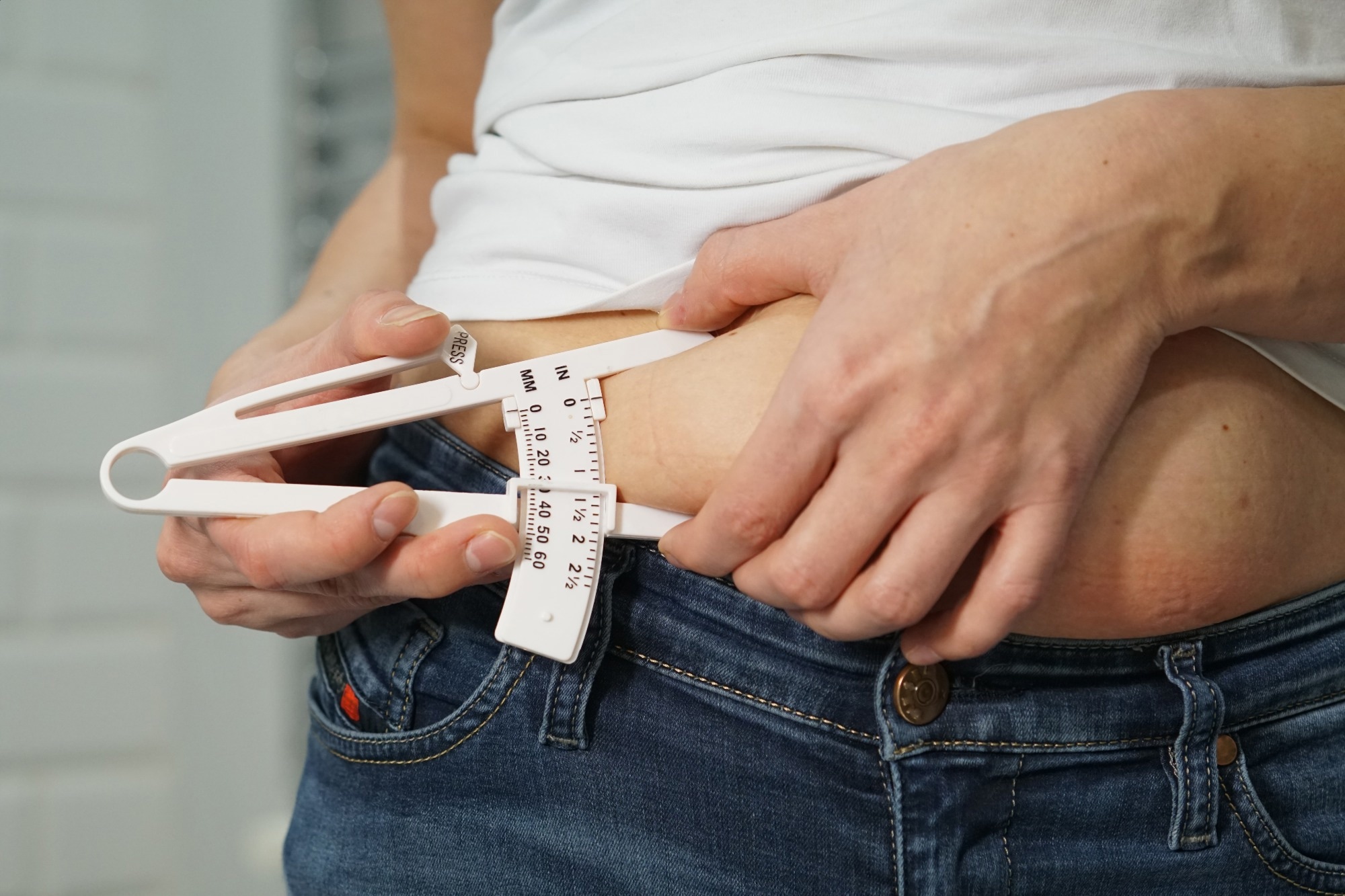 A woman in a white T-shirt and navy blue jeans measures the level of body fat with a special device