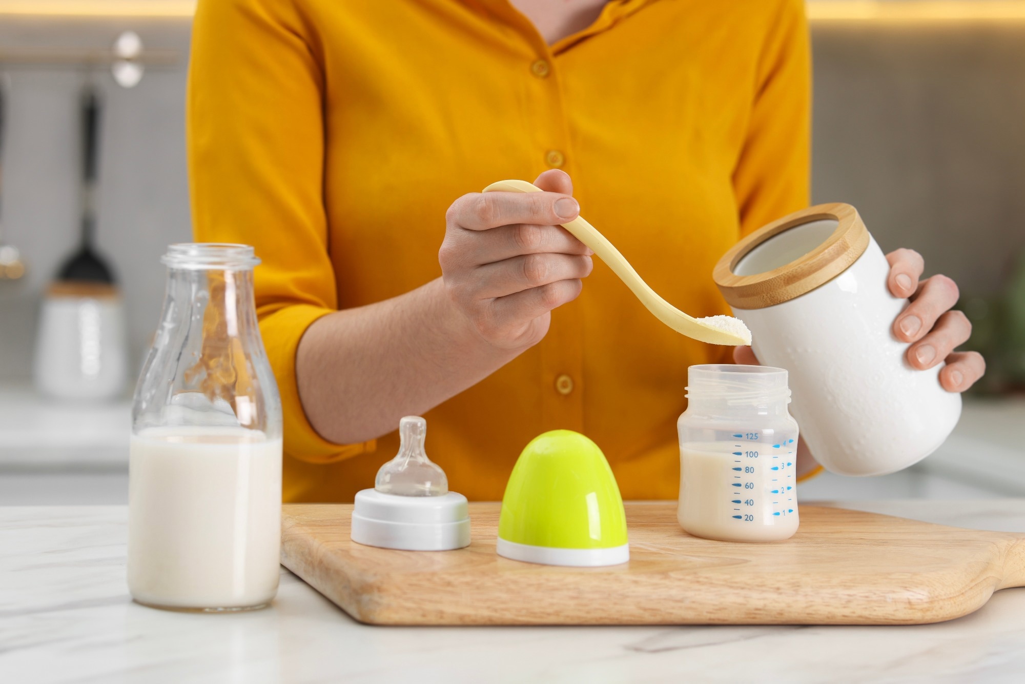 Mother making baby formula in feeding bottle at table