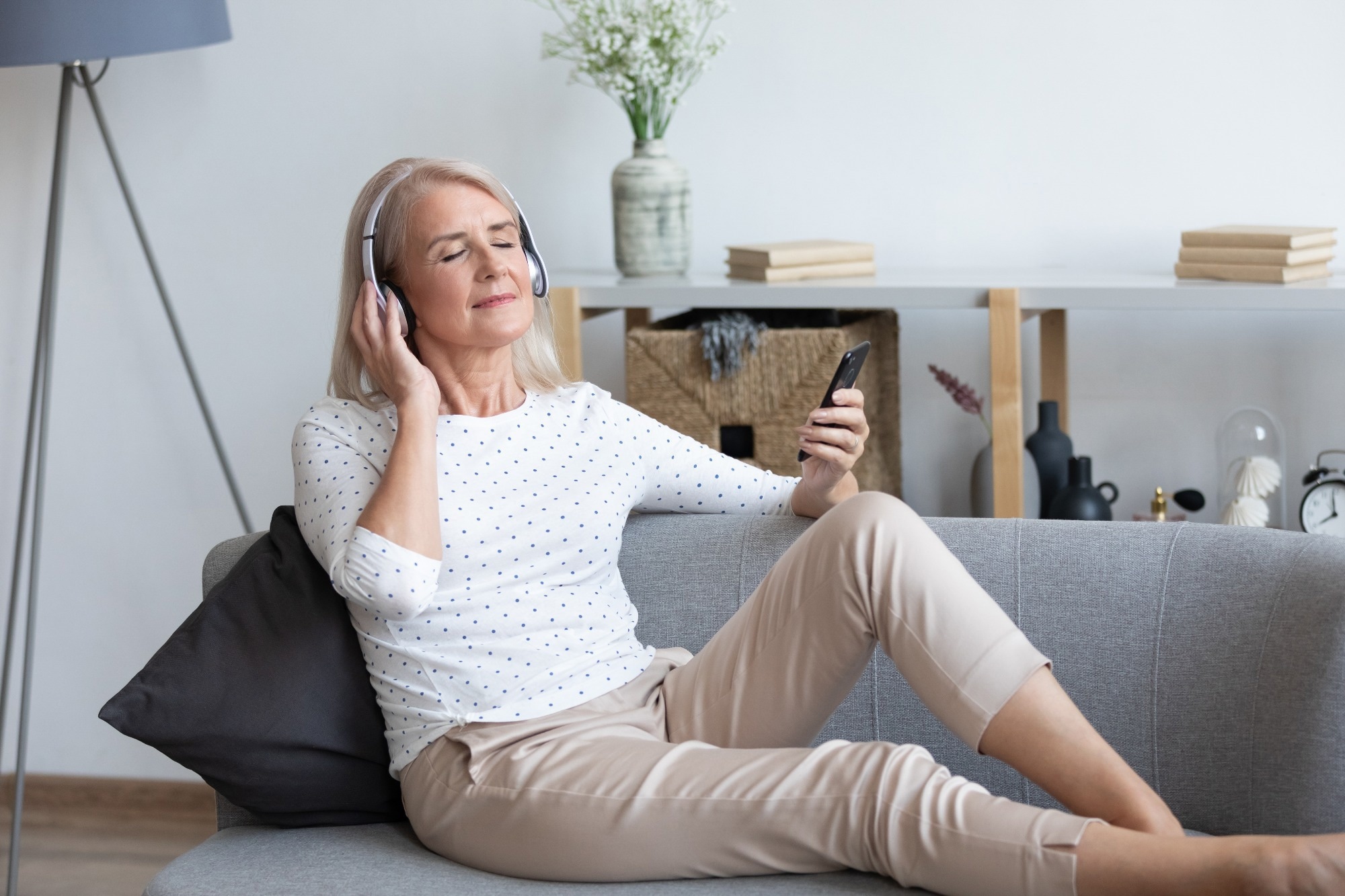 Older adult lady with headphones on, relaxed in sofa