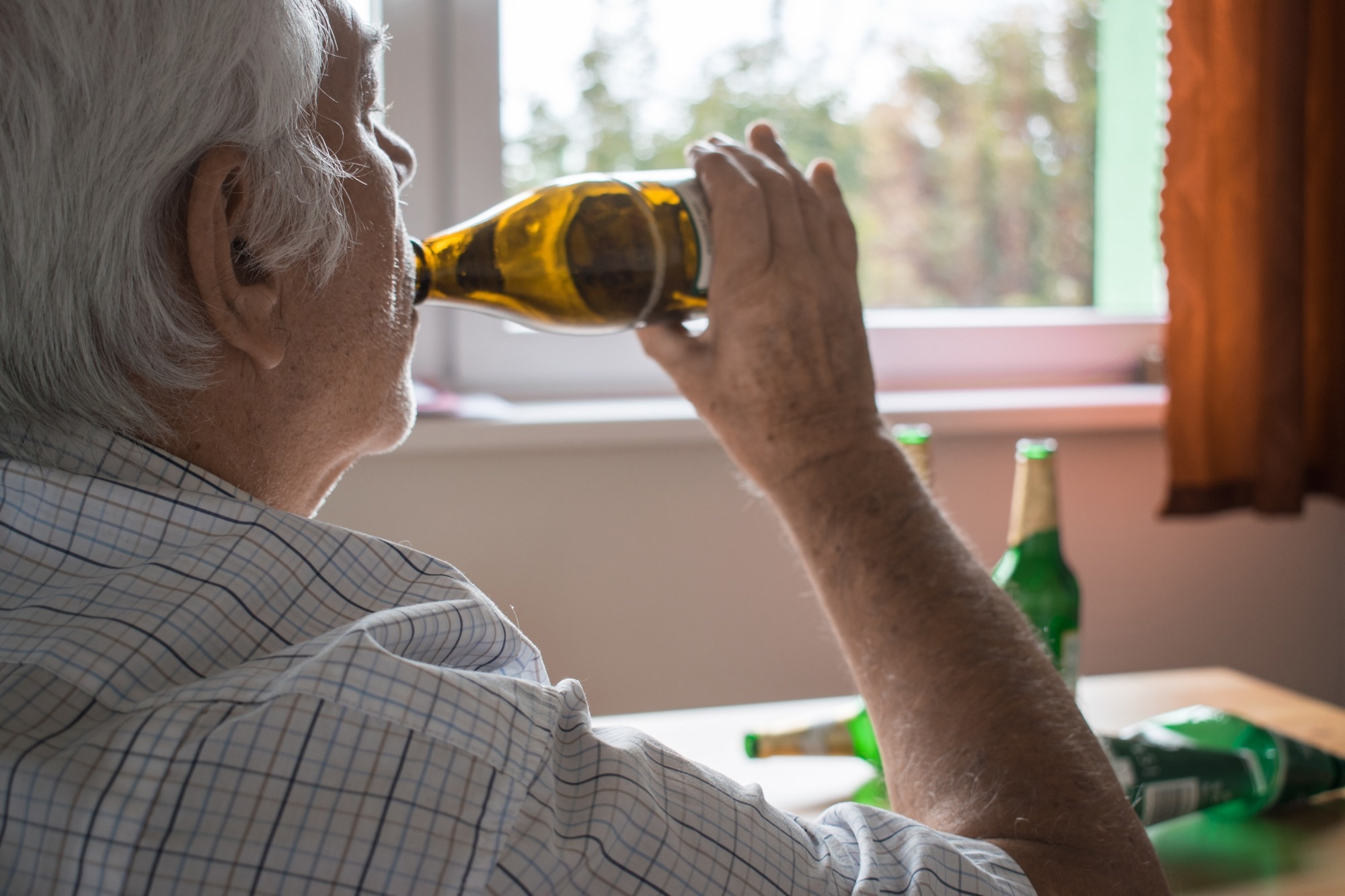 old senior man sit next to table drink alcohol bottle at home
